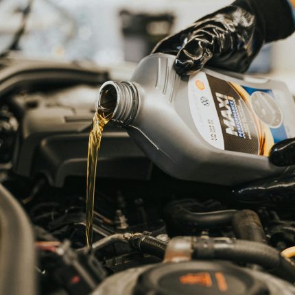Close-up of a mechanic's gloved hand pouring engine oil into a vehicle.