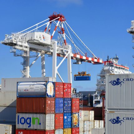 Colorful shipping containers stacked in a busy port with cranes overhead.
