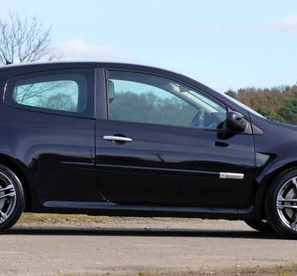A black Renault Clio RS parked in a natural setting with trees.