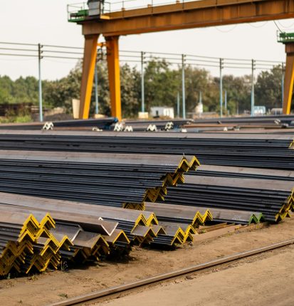 Numerous steel beams neatly stacked in an industrial yard during daytime.