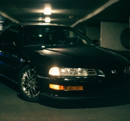 A black Honda car with headlights on, parked in an indoor garage, showcasing sleek design.